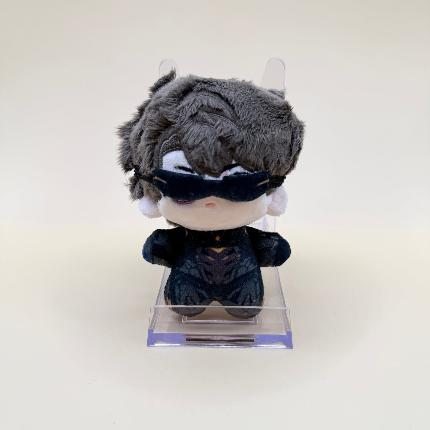 Plush toy with gray hair and black outfit on a clear stand against a white background